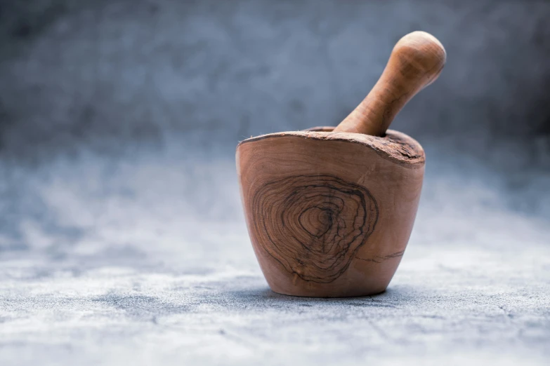 a hand carved mortar in a bowl, the mortar has a handle