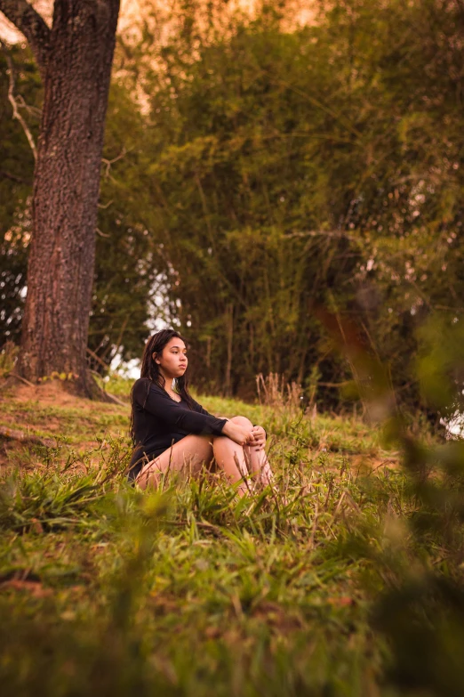 a beautiful young woman sitting in the grass next to trees