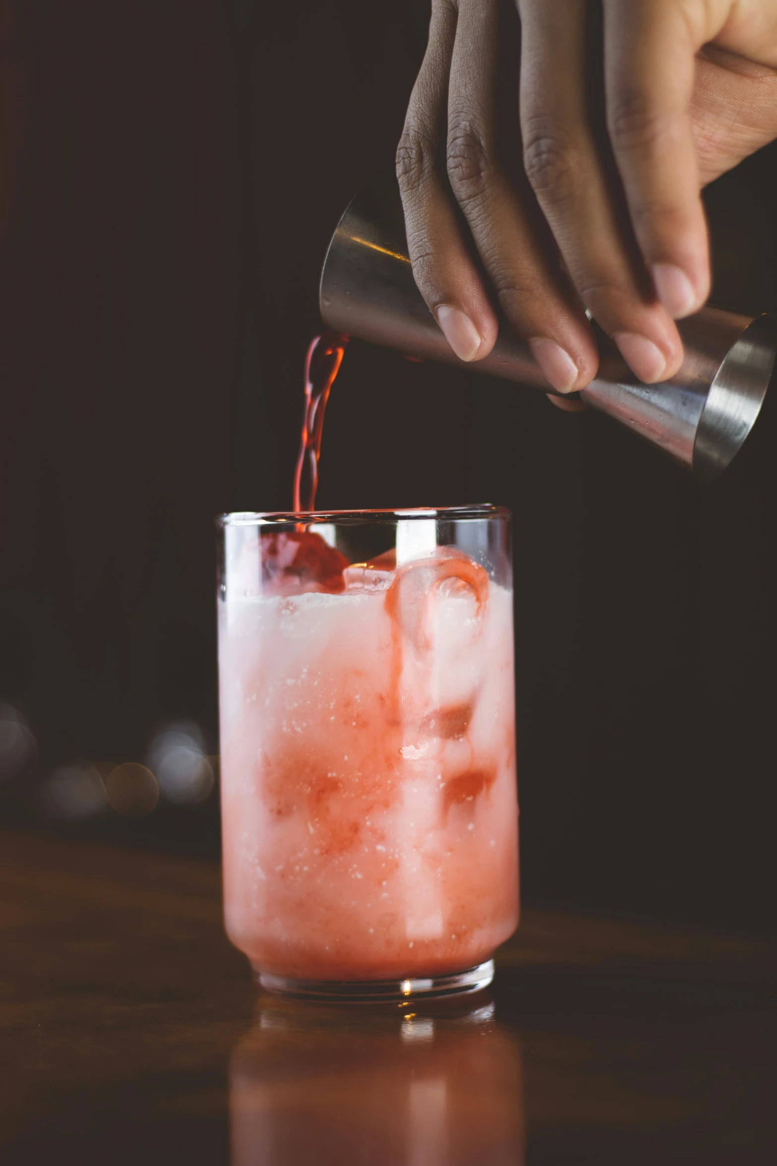 a person pours cocktail into a glass