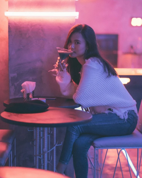 an attractive woman sitting down and drinking from a glass