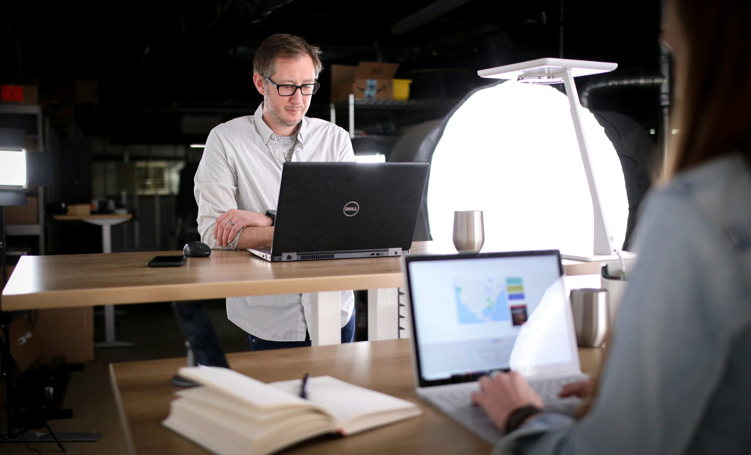 a man at a desk on a laptop looking over an open book