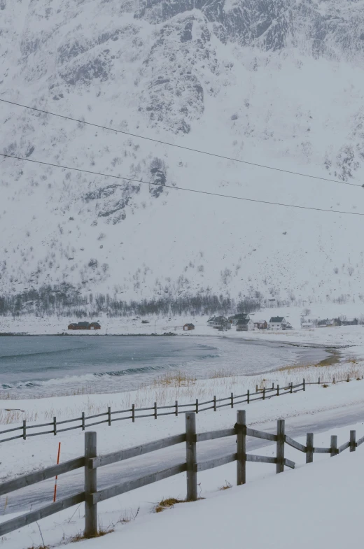 snow covered field and mountains by fence near waterway