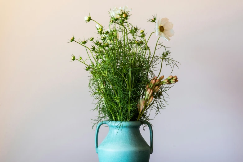 some daisies and weeds are in a teal blue vase