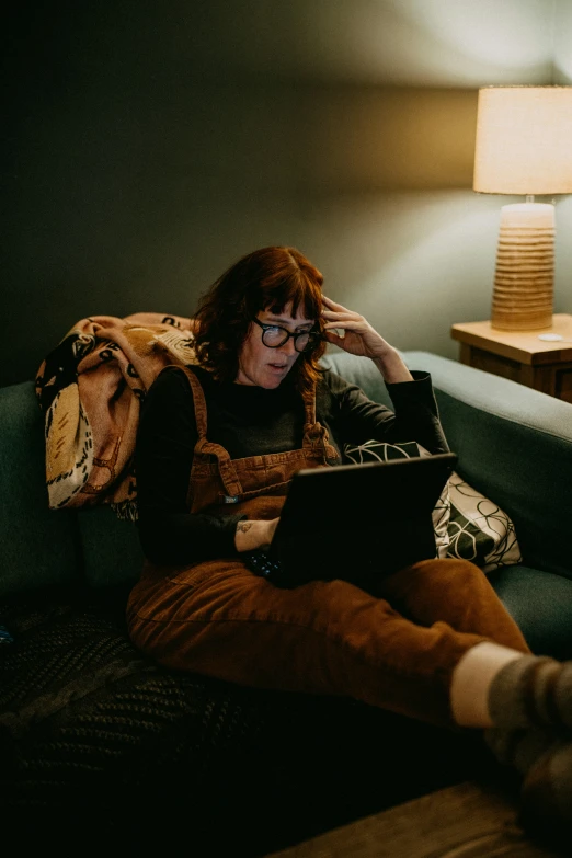 the woman sits on the couch with her legs crossed, looking at her laptop