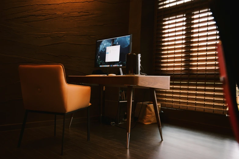 a desk with computer on top of it and wooden blinds