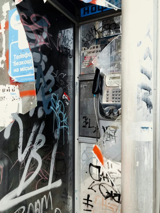 a phone booth is covered in graffiti near a telephone pole