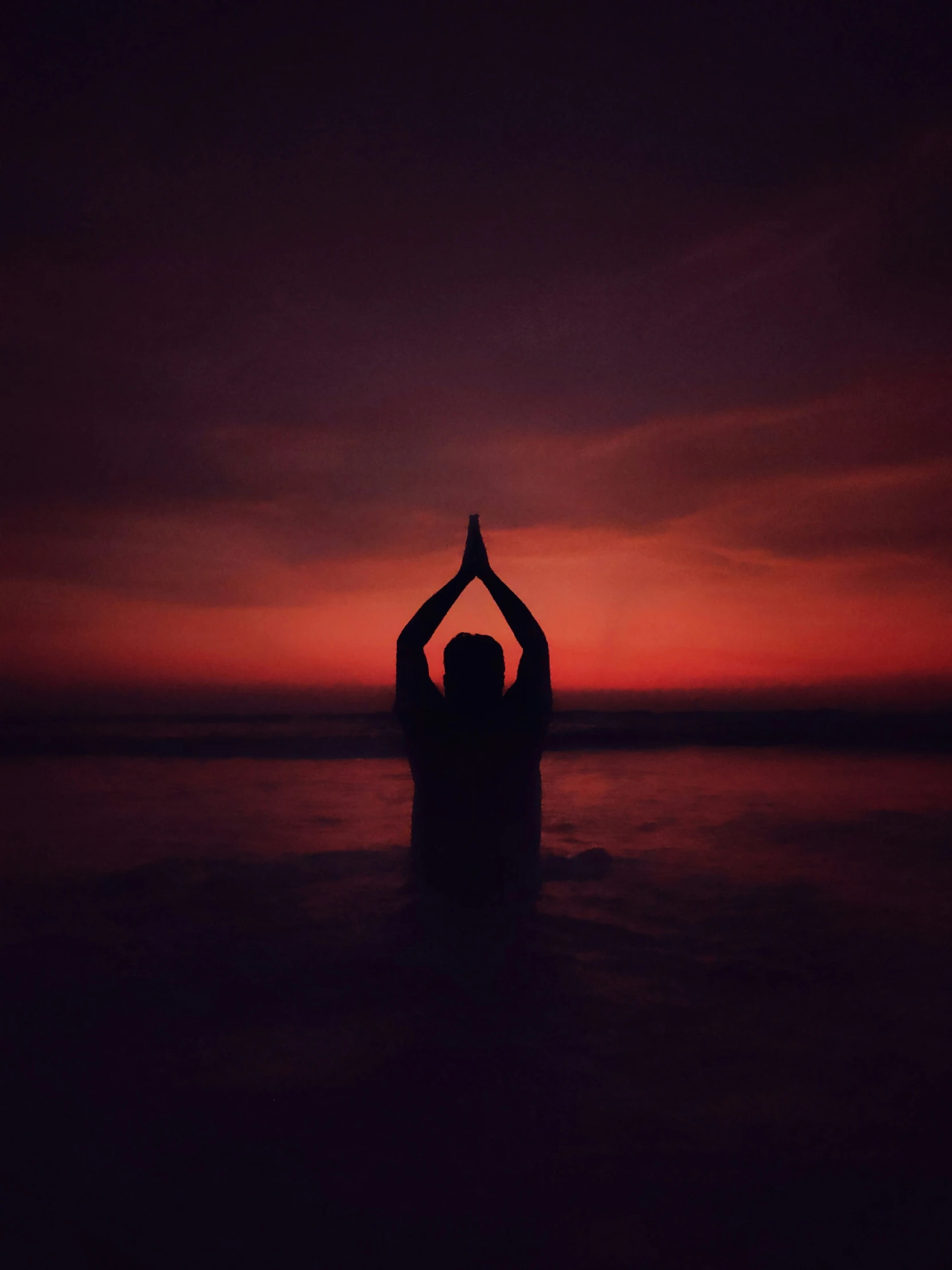 person in silhouette on the edge of body of water during sunset