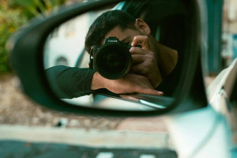 the side view mirror on a car shows a man holding a camera