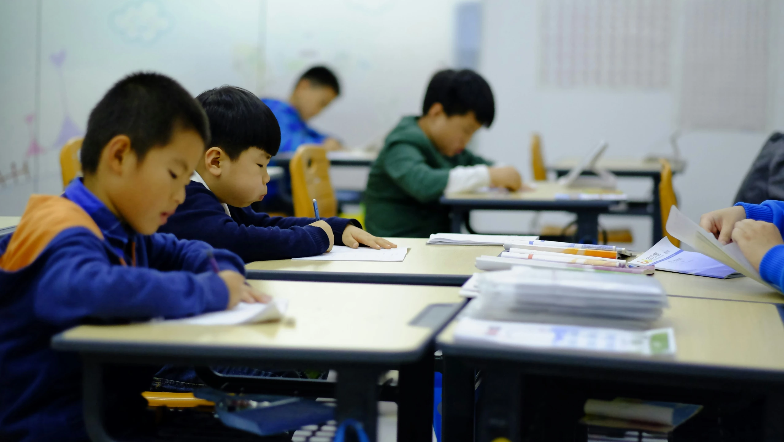 four children in classroom sitting at desks with books