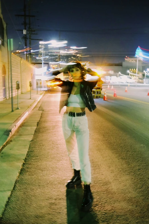 a woman wearing white pants standing on a sidewalk with an umbrella over her head