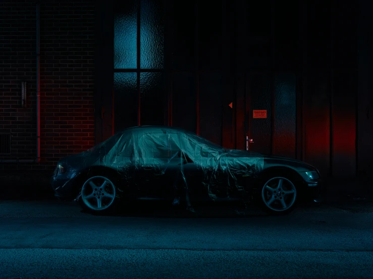 a car covered in a tarp is parked on the side of the street at night