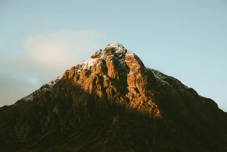 a very tall mountain in the sunlight with a sky background