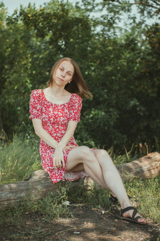 young woman in red dress sitting on log in outdoor setting