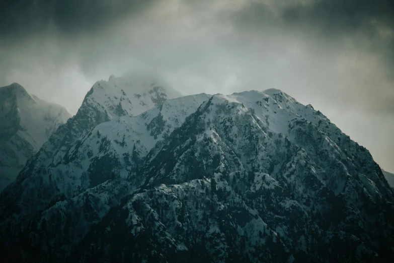 a very tall mountain covered in snow under a cloudy sky