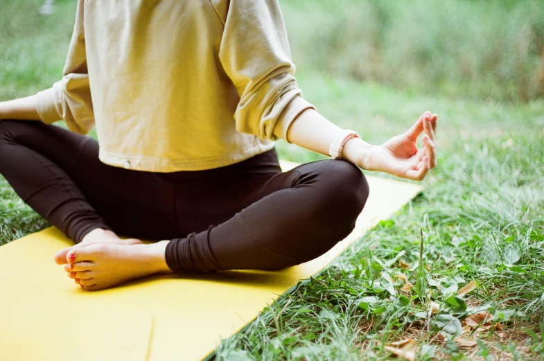 a woman is meditating on a mat in a park
