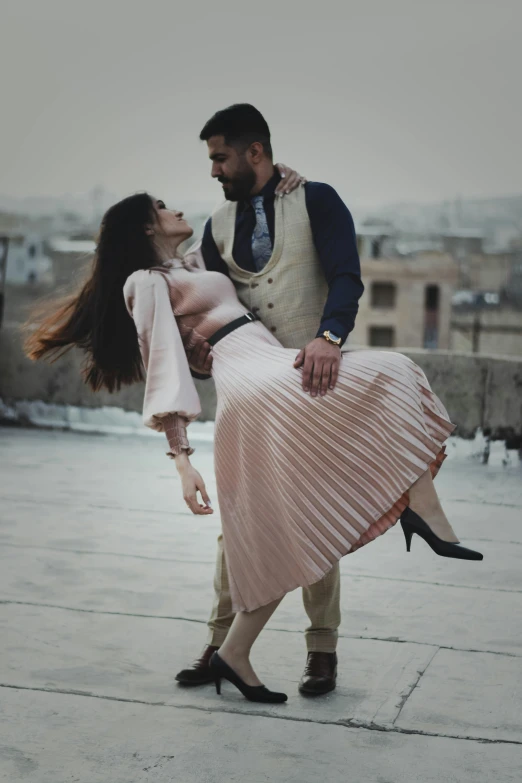 a woman on stage, holding onto a man as he has a pleated dress with pleating detailing