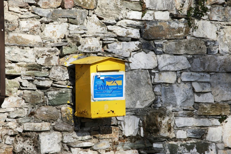 a yellow mailbox sitting on top of a stone wall