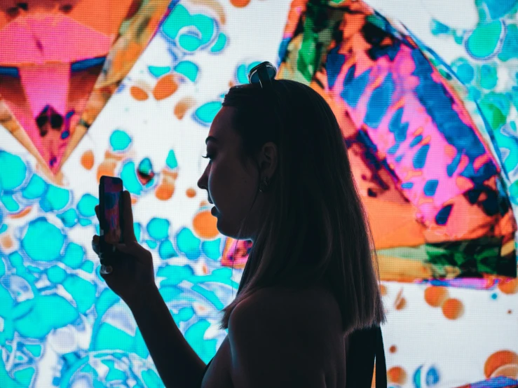 a woman holds up a cell phone with a painting on it