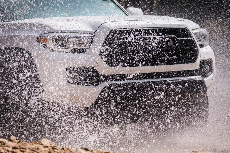 the front of a white truck that is splashing in sand