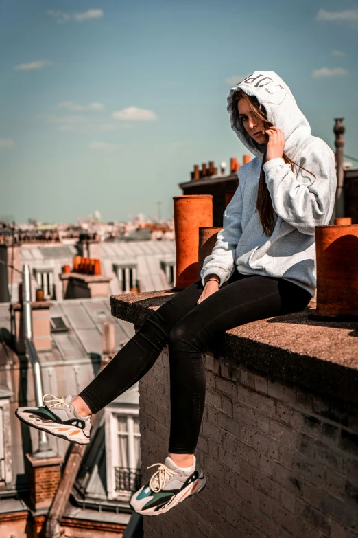 a woman sitting on a wall wearing sneakers and talking on her cell phone