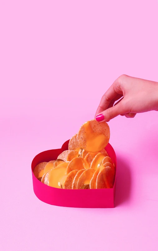 a hand grabbing a donut out of a pink heart box