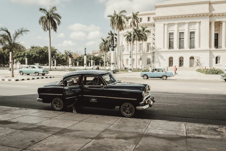 two classic cars are parked on the sidewalk in front of a large building