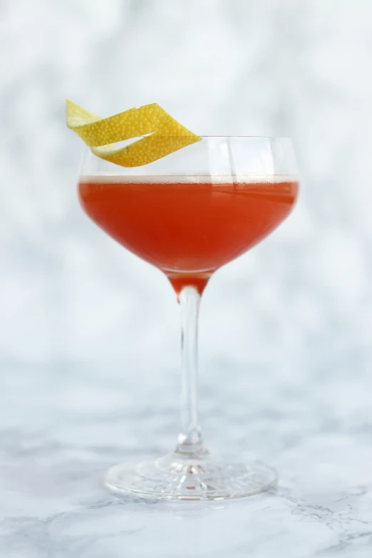 a red cocktail in a glass with a yellow garnish