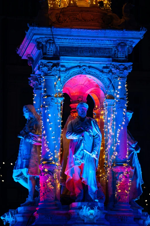 lighted outdoor sculpture with man sitting on a stage