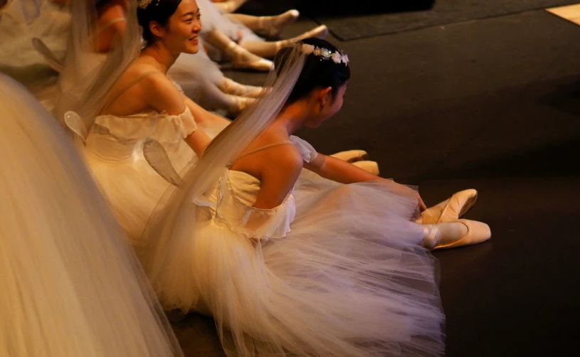 several girls dressed in wedding garb sit and look at the floor