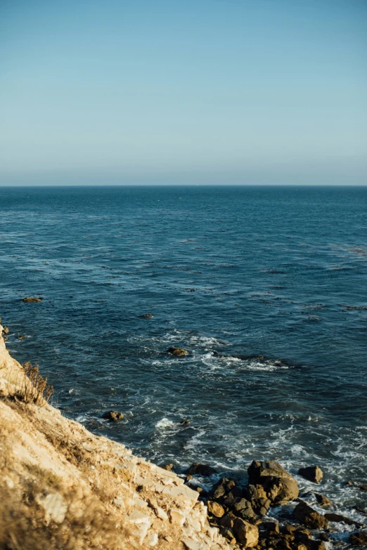 a surfboarder walking on the edge of a cliff next to the ocean
