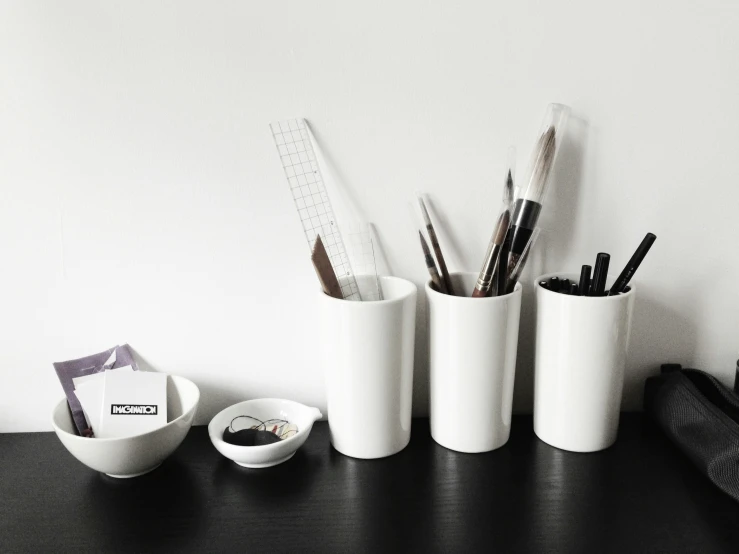 white desk with several pen, pencils and cups