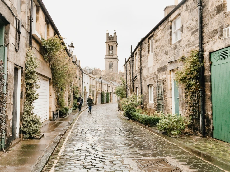 two people walk down an old cobble stone road with green doors