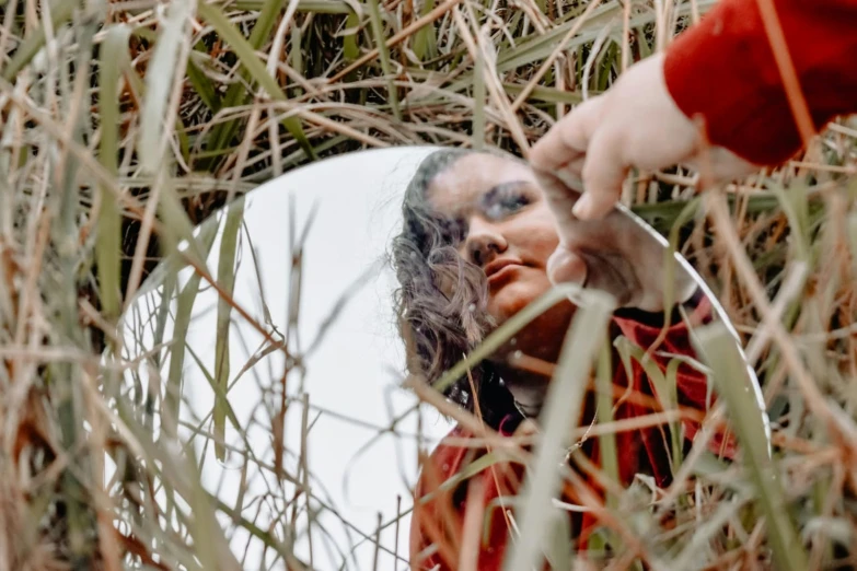 a girl in a red sweater in tall grass with her hand on the mirror