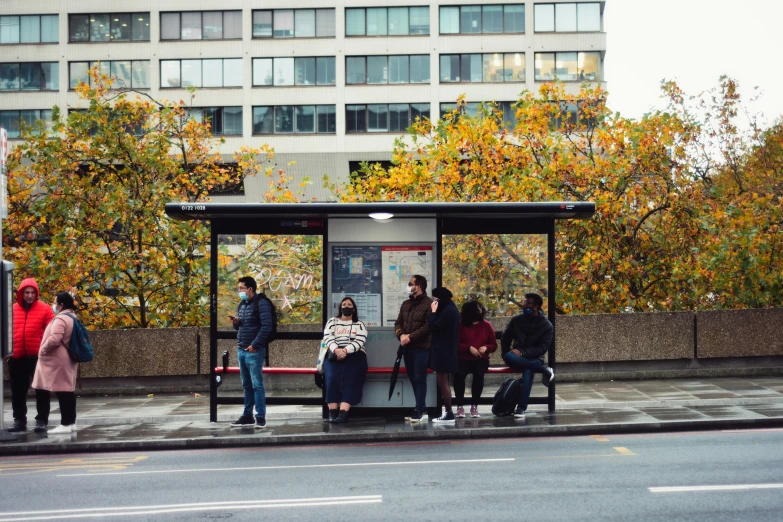 group of people sitting on a bench next to a bus stop