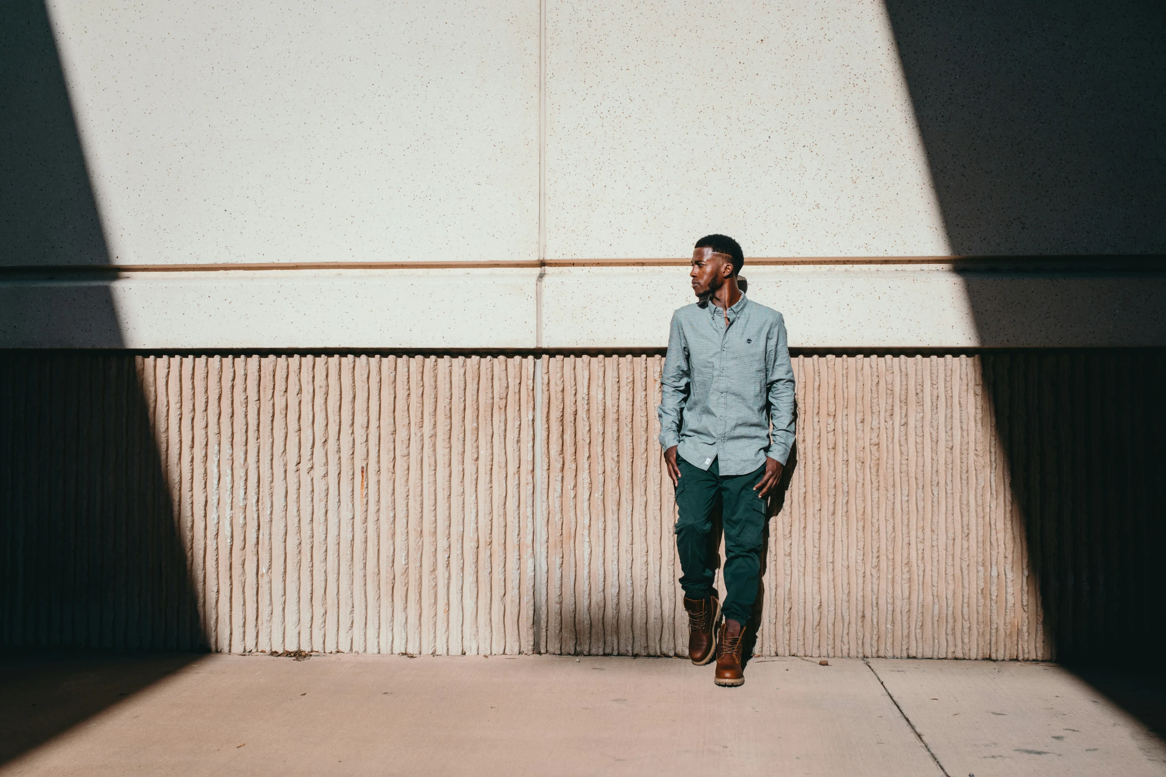 a man stands in the shadows wearing a blue shirt