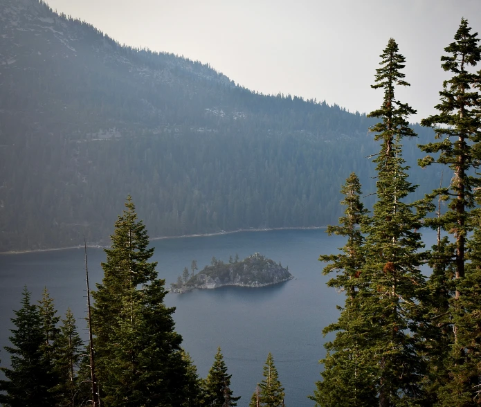 a small island sits in the middle of a mountain lake surrounded by pine trees