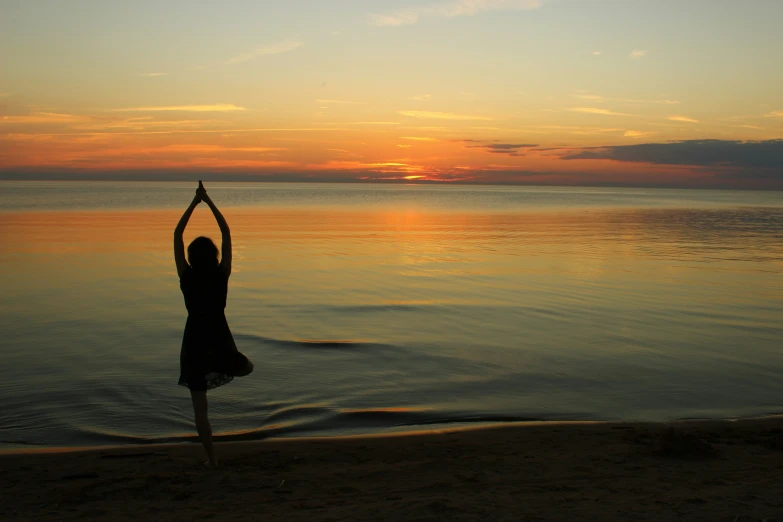 a person doing yoga on a beach with their arms in the air