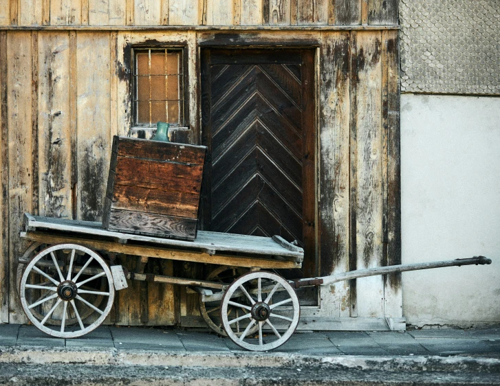 an old wooden wagon with a broken door sitting on the side of a building