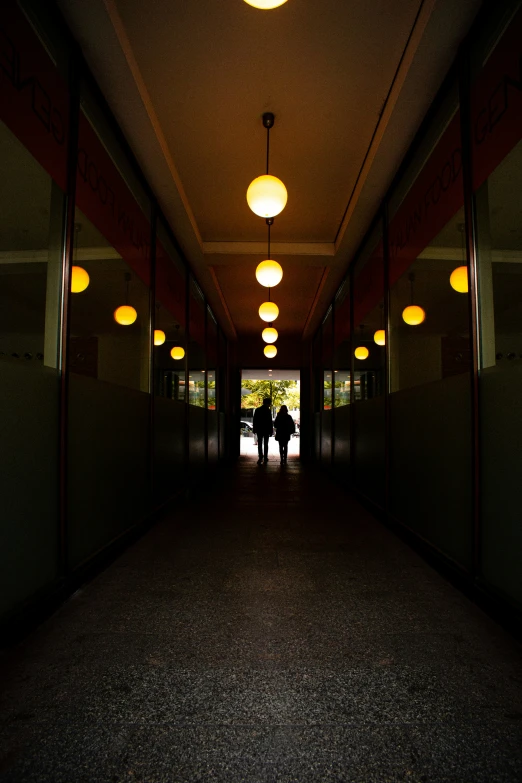 two people are standing in a dark hallway with many lamps above them