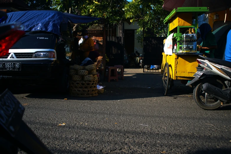 a small street side with a cart, scooter and a yellow truck