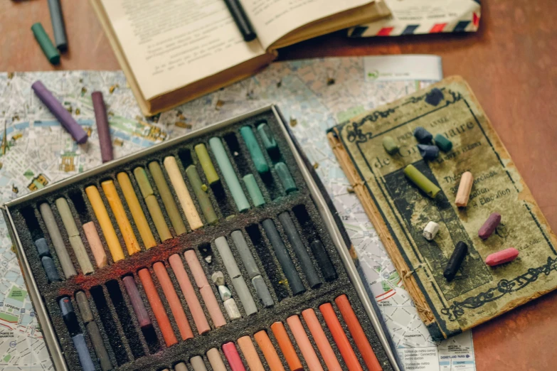 a box of colored crayons on a table next to an open book