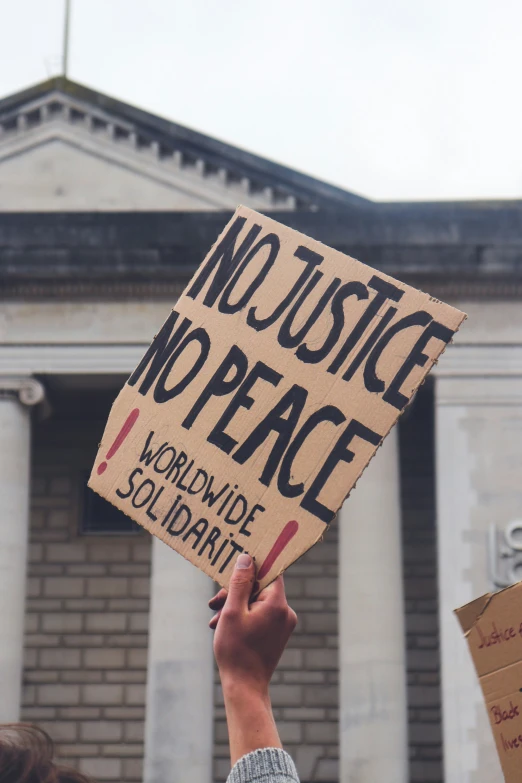 protest sign in hand against building with crowd holding sign