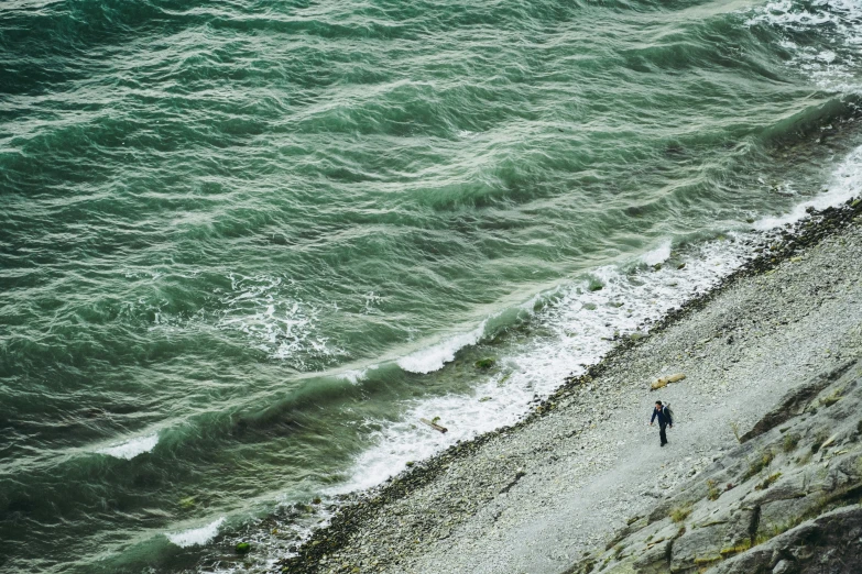 two people walking near the ocean shore with one person holding an umbrella