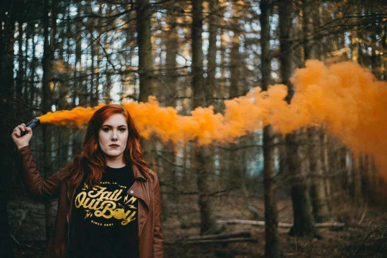 a young woman is blowing yellow smoke into the woods
