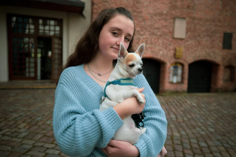 girl in blue sweater holding dog on brick walkway