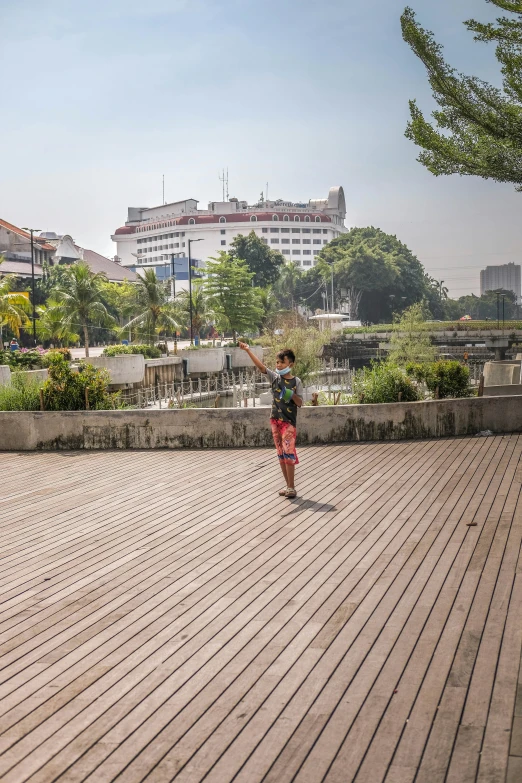 the man is walking along on the boardwalk by the city