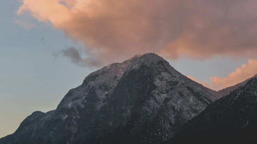 the mountain top is covered with snow as it sits under a cloudy sky