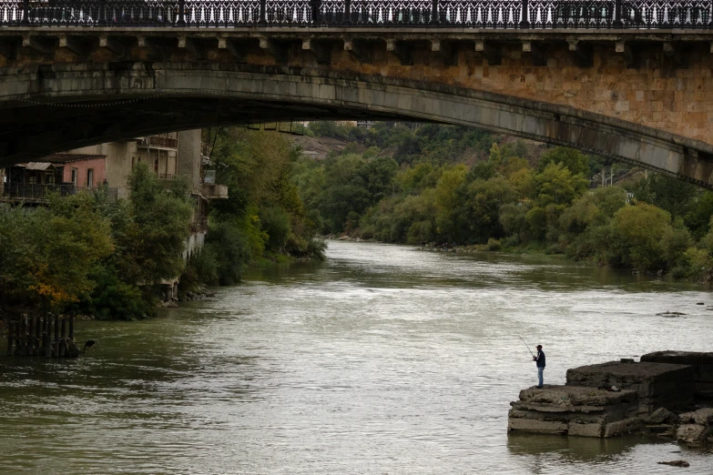 a man is standing in the river with a bridge in the background