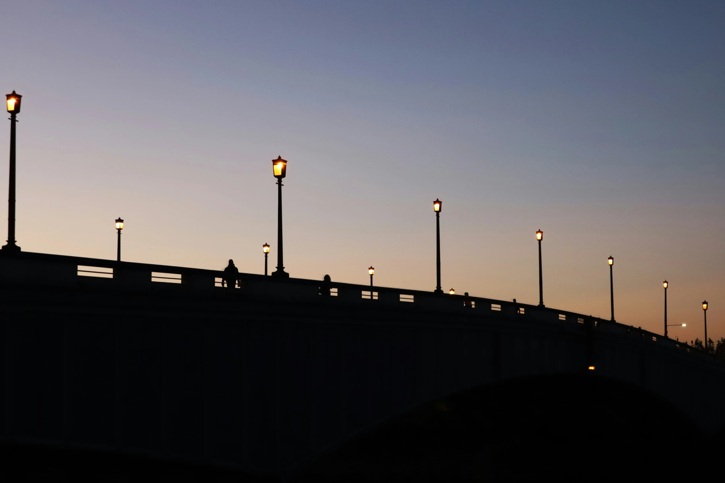 the lamp posts shine bright as people walk down the bridge