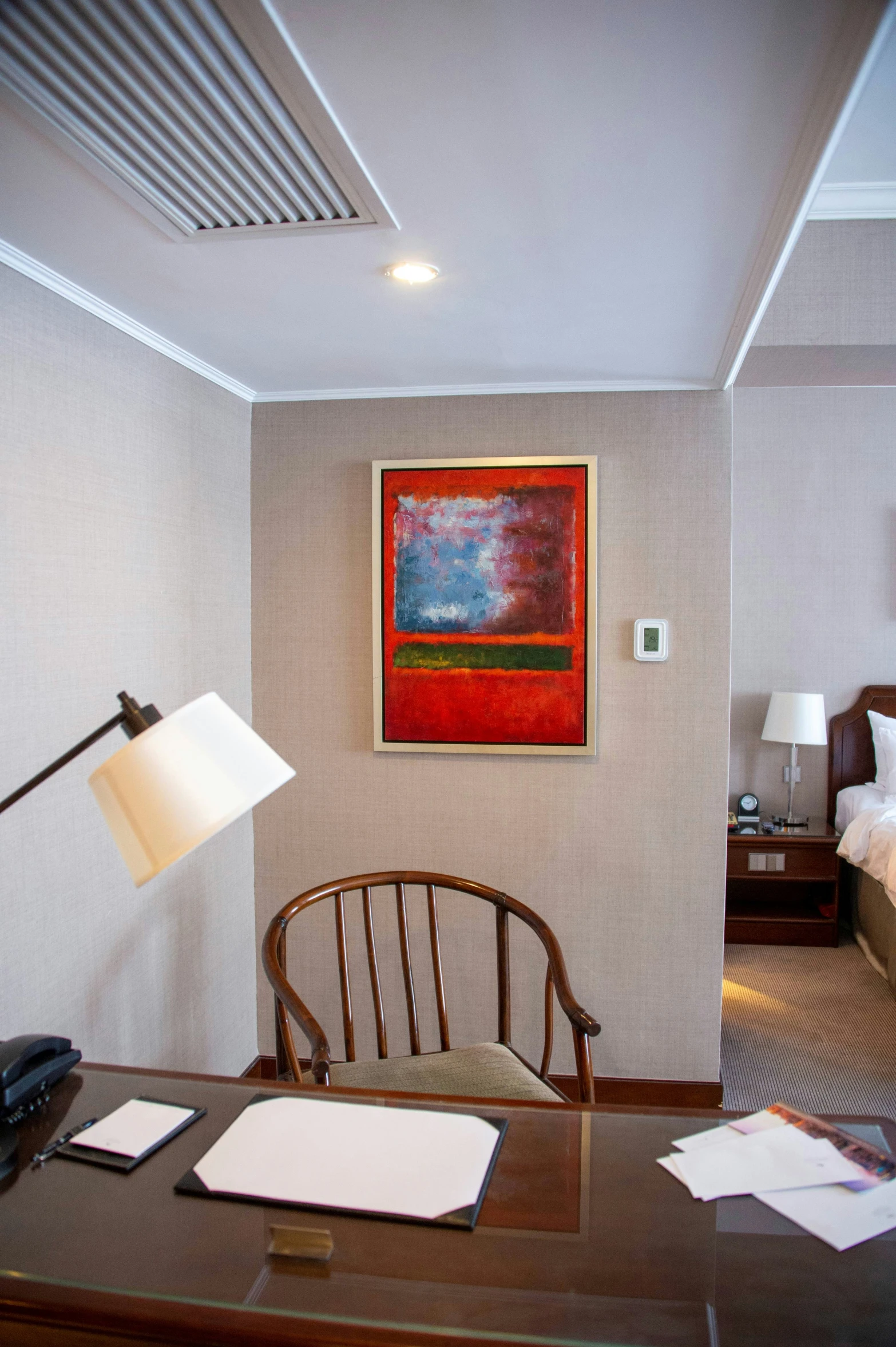 a desk with a chair, lamp, and a painting hanging on a wall